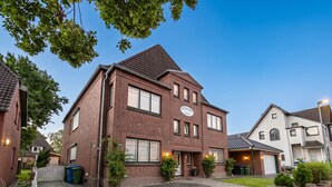 A two-story brick house with a garage, surrounded by a paved driveway and greenery. - Gode Stuv: Cozy vacation rental with a balcony (Büsum)