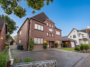 Ein zweistöckiges Backsteinhhaus mit Garage, umgeben von einer gepflasterten Auffahrt und Grünflächen.