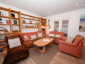 A living room with a sectional sofa, a wooden coffee table, and a bookshelf filled with books and decorative items. - Gode Stuv: Cozy vacation rental with a balcony (Büsum)