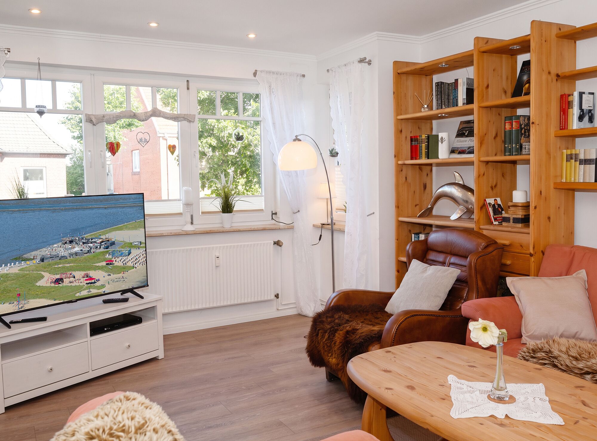 Een gezellige woonkamer met een televisie, een boekenkast, een leren fauteuil en een houten salontafel.