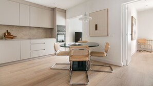 Una cucina moderna con mobili bianchi, un'area pranzo con un tavolo in vetro e sedie in metallo, e una lampada a sospensione.