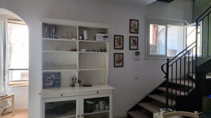 A staircase with a black railing leading to an upper floor, a white shelving unit with various items, and a window with a view of the outside. - Bright apartment in the heart of Vicenza with a view of the Basilica Palladiana (Vicenza)