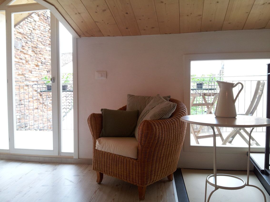 Un canapé en osier avec des coussins, une table blanche et une vue sur un bâtiment en briques, visible à travers une porte vitrée.