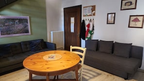 Ein Wohnzimmer mit einem runden Holztisch, zwei Sofas, einem Heizkörper und einer Tür mit einem Zettel.