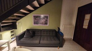 A room with a grey sofa, a staircase, a framed picture on the wall, and a radiator. - Bright apartment in the heart of Vicenza with a view of the Basilica Palladiana (Vicenza)