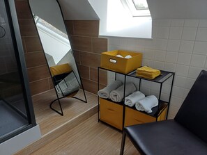 Ein Badezimmer mit Spiegel, einem schwarzen Stuhl, einem Handtuchregal und einer gelben Aufbewahrungsbox.