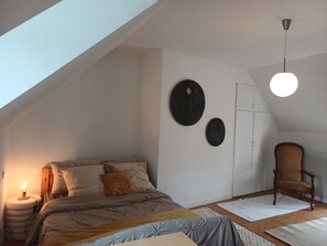 A bedroom with a sloped ceiling, a bed with multiple pillows, a chair, and two wall-mounted circular decorations.