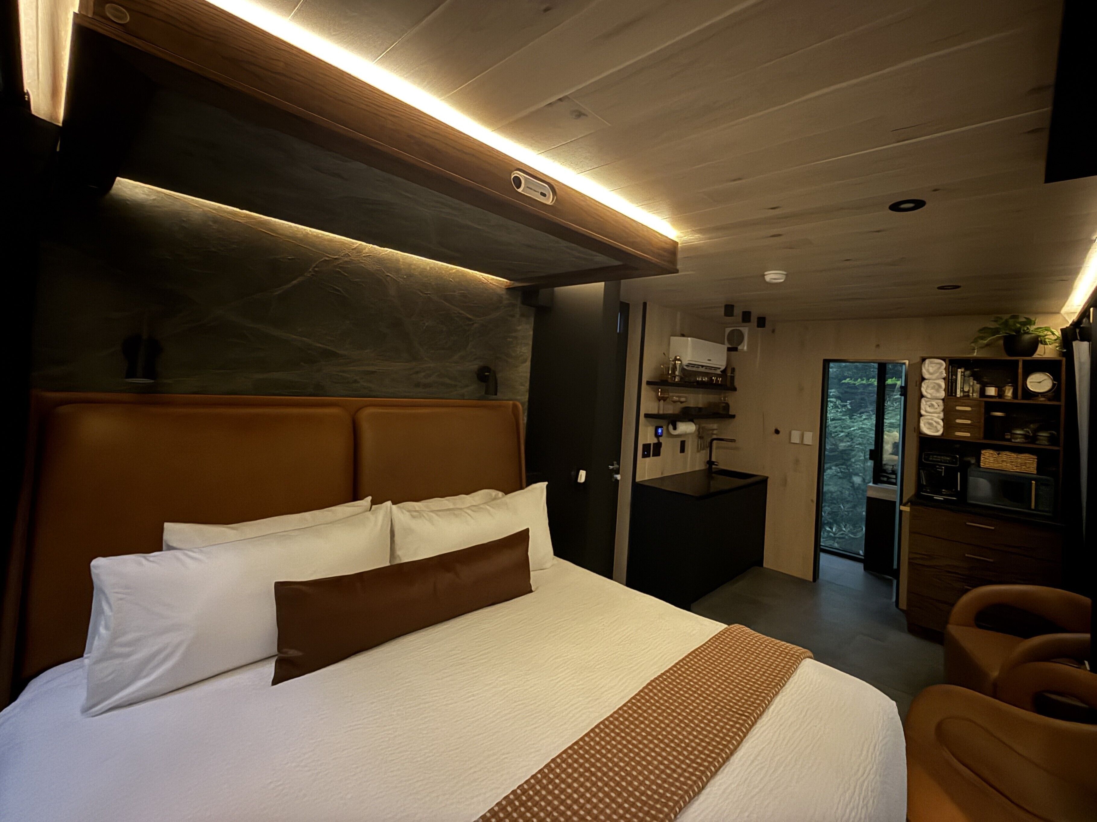 Une chambre moderne avec un grand lit, une tête de lit en bois, un bureau intégré et une vue sur l’extérieur.