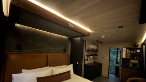 A modern bedroom with a large bed, a wooden headboard, a built-in desk, and a view of the outdoors. - Mirror house wellness retreat: private sauna, hot tub, spring-fed cold plunge & your own waterfall. Tucked on 35 acres along the French Broad River, minutes from Brevard breweries, Pisgah & DuPont. (Pisgah Forest)