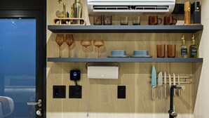A modern kitchen with a marble countertop, built-in shelves with kitchenware, a wall-mounted air conditioner, and a digital clock. - Mirror house wellness retreat: private sauna, hot tub, spring-fed cold plunge & your own waterfall. Tucked on 35 acres along the French Broad River, minutes from Brevard breweries, Pisgah & DuPont. (Pisgah Forest)