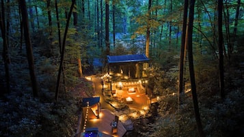 Una cabaña aislada en un bosque con jacuzzi, mobiliario exterior y una terraza.