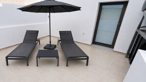 A balcony with two sun loungers, a small table, and a black umbrella. - Zidros Apartments Maisonette Apartment 3 (Sfakaki)