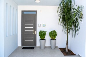 Une entrée moderne avec une porte grise, des plantes en pot et une enseigne fixée au mur.