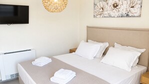 A hotel room with a bed, a flat-screen TV mounted on the wall, a radiator, and a painting of flowers. - Zidros Apartments Maisonette Apartment 3 (Sfakaki)