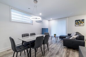 A modern living room with a dining table, sofa, and a painting on the wall. - Modern 2BR Basement Suite Near Montreal, Free Parking & WiFi (Longueuil)