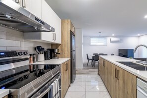 A modern kitchen with stainless steel appliances, wooden cabinets, and a large island with a sink. - Modern 2BR Basement Suite Near Montreal, Free Parking & WiFi (Longueuil)