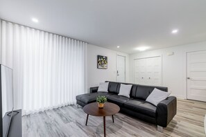 Ein modernes Wohnzimmer mit einem schwarzen Ledersofa, einem runden Holztisch und einem weißen Vorhang.