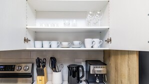 Ett kök med vita skåp, en kaffebryggare och diverse köksredskap.