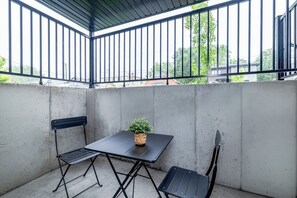 Eine kleine Terrasse im Freien mit Tisch und zwei Stühlen, einem Blumentopf und Blick auf die Nachbarschaft.