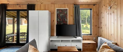 A wooden cabin interior with a sofa, TV, and storage unit.