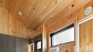 Een badkamer met houten lambrisering, voorzien van een douche, toilet en wastafelmeubel.