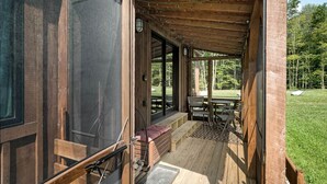 Een houten terras met een bank, een tafel en uitzicht op een grasveld.