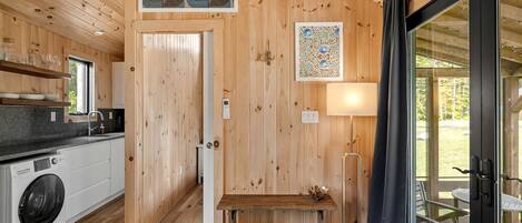 Un interior de madera con cocina, un banco, una mesa y vistas a través de un ventanal.