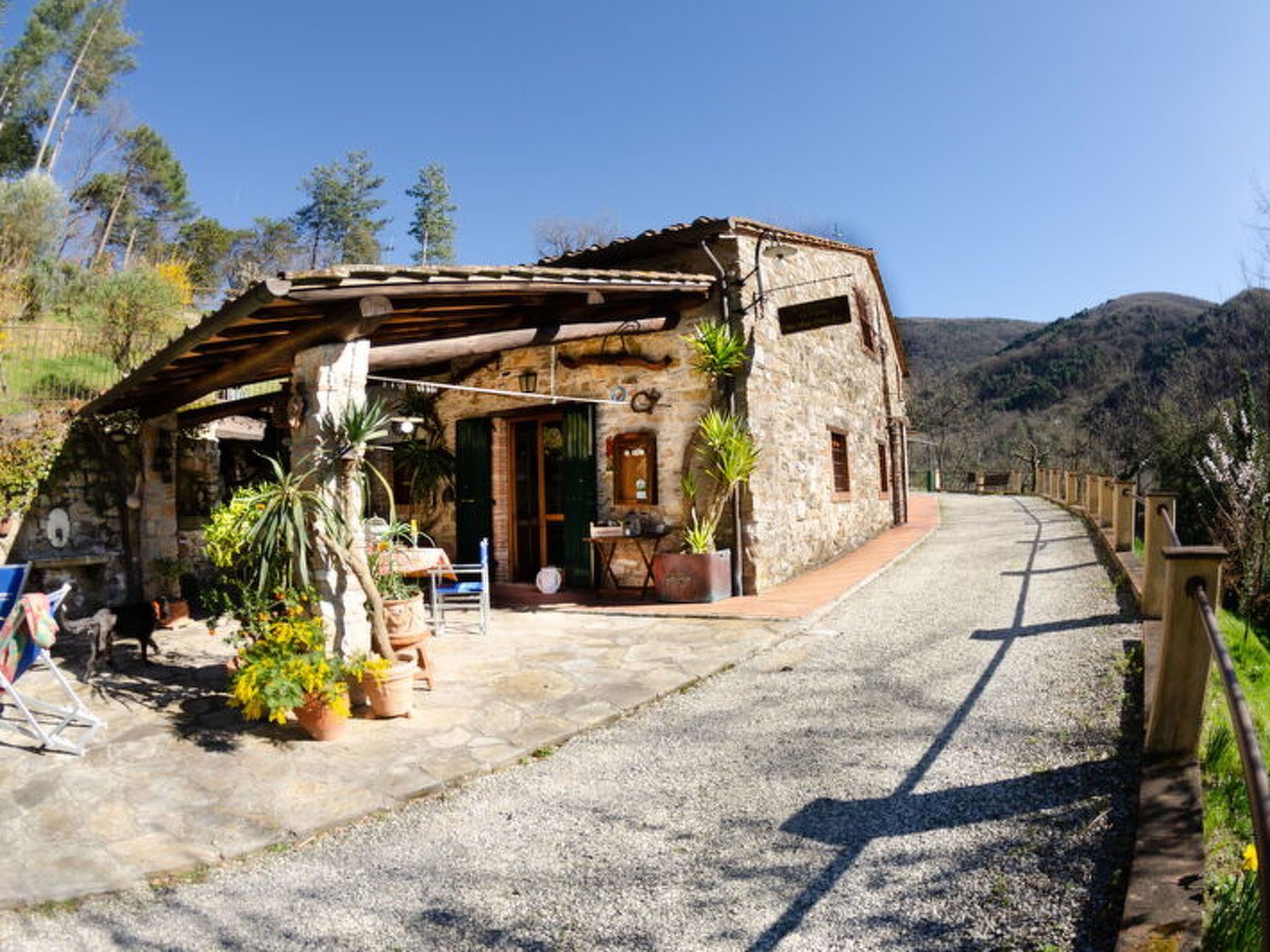 A rustic stone building with a covered outdoor seating area, a gravel path, and a mountainous backdrop.