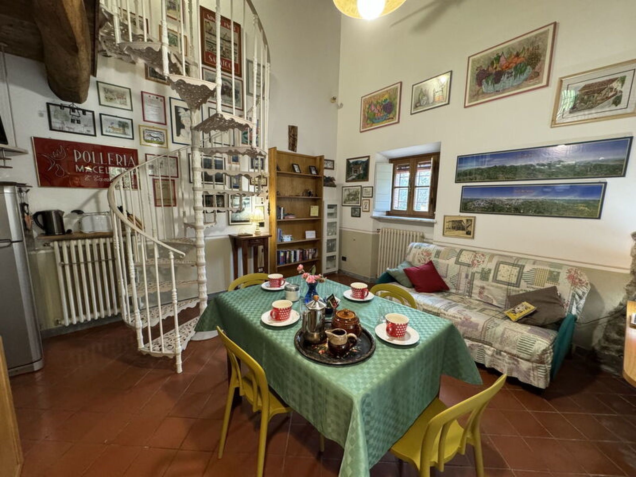 A dining area with a table set for four, a spiral staircase, and a sofa with a view of the countryside.