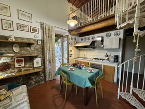 A cozy kitchen with a dining table set for four, a stone wall with shelves, and a staircase with a balcony. - Le Piane by Interhome (Lucca)