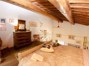 A room with a wooden ceiling, a bed with a floral bedspread, a wooden dresser, a chair, and a small table with a lamp. - Le Piane by Interhome (Lucca)