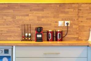 Una cocina con protector mural de madera, una cafetera, dos recipientes rojos y un reloj.