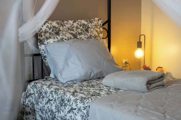 A bed with a floral bedspread, a white pillow, and a grey blanket.