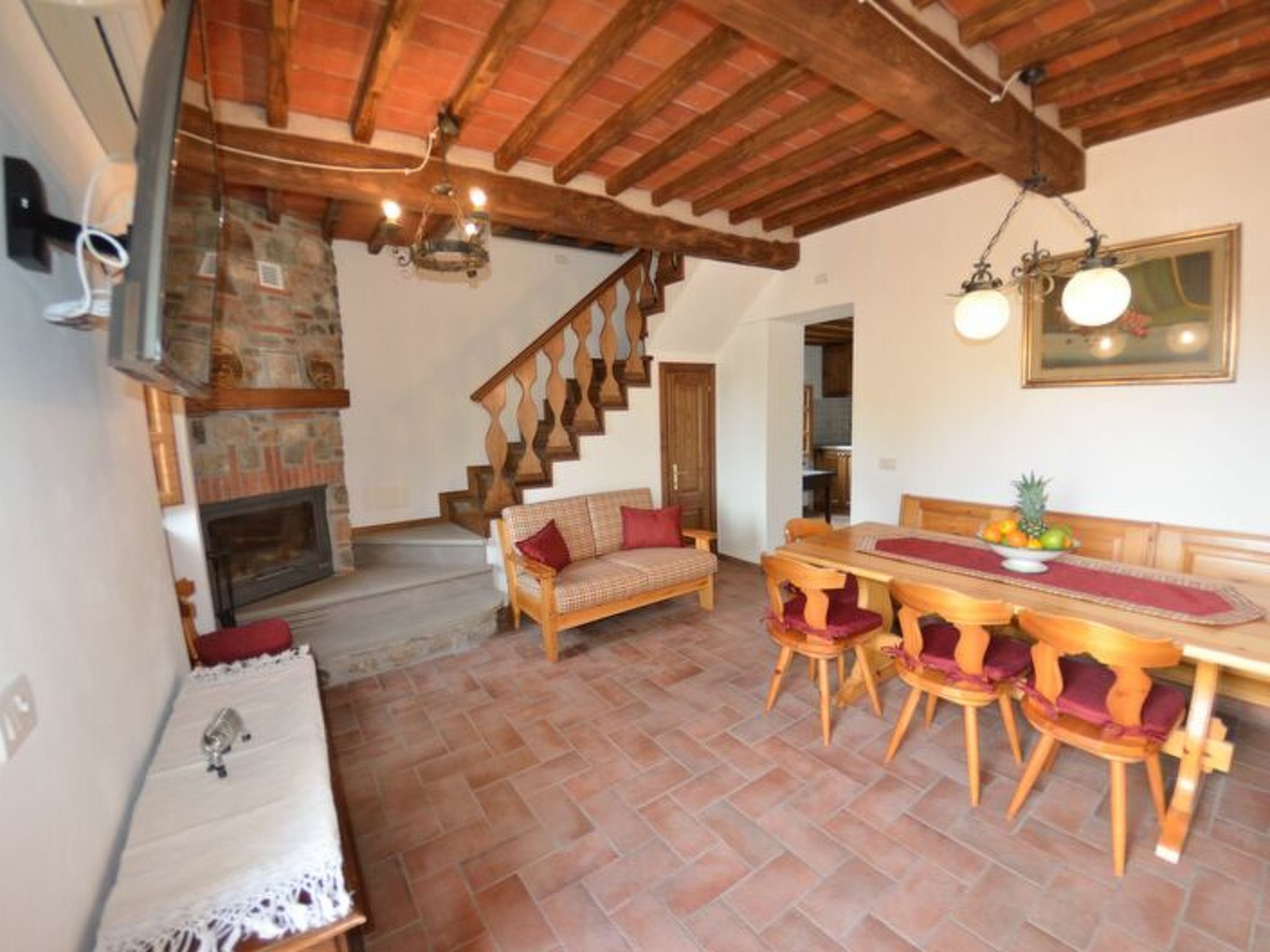 A rustic interior with a stone fireplace, wooden staircase, and a dining area with a wooden table and chairs.