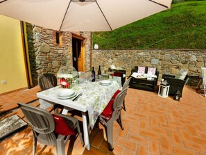 Uma área de refeições ao ar livre com um fundo de parede de pedra, uma mesa posta para dois e um espaço de estar acolhedor.