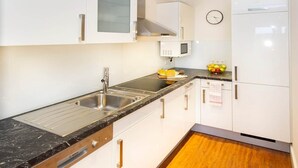 A modern kitchen with white cabinets, a black countertop, a stainless steel sink, and a microwave. - Feuerstein Family Home, Apartment 4 (Wangerooge)