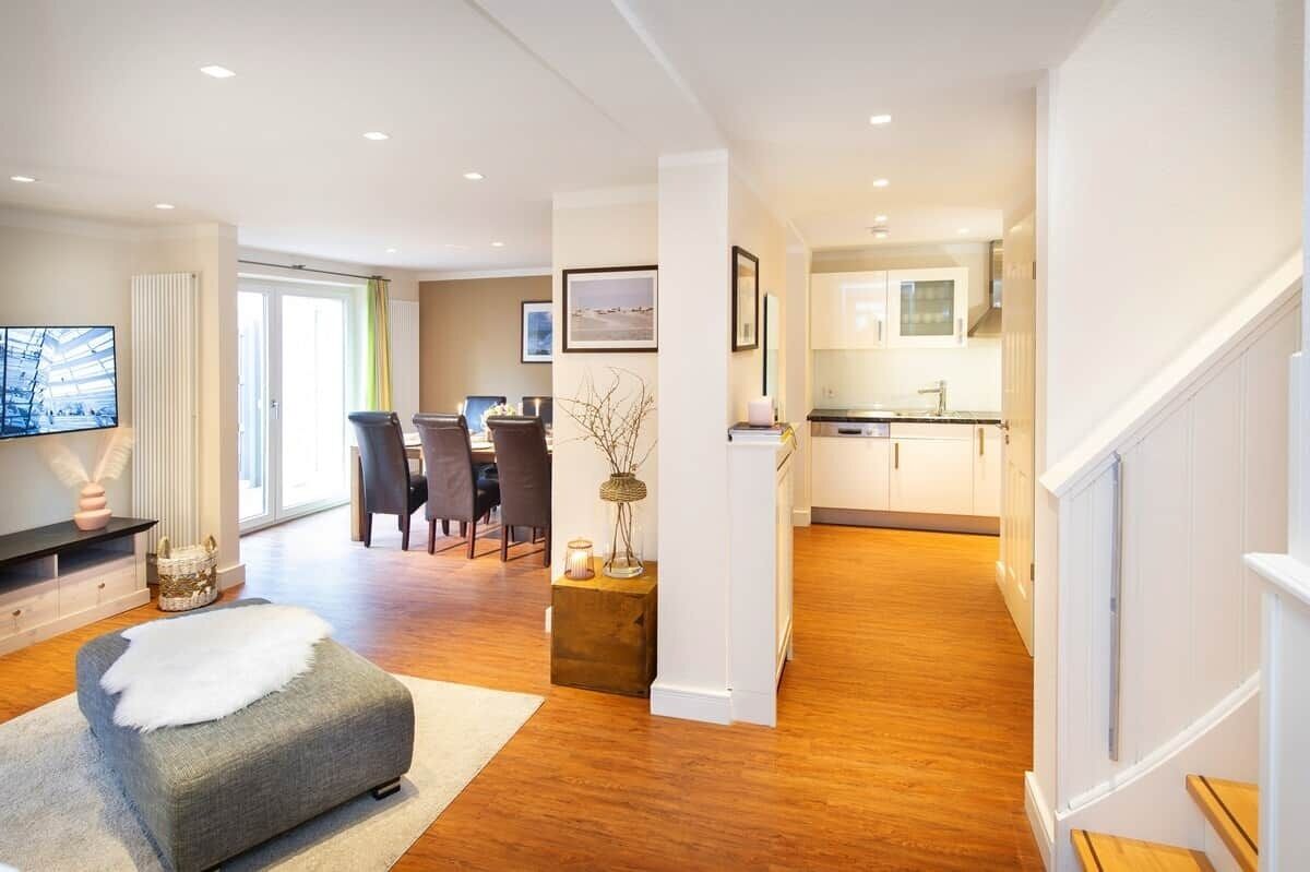 Een moderne woonkamer met een grijze bank, een eethoek met stoelen en een keuken met witte kastjes.