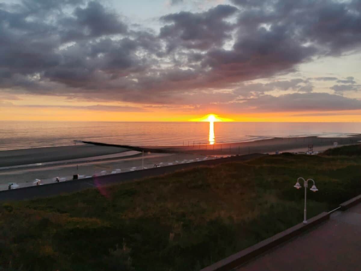 Un coucher de soleil sur une zone côtière, avec une route et une berge herbeuse.