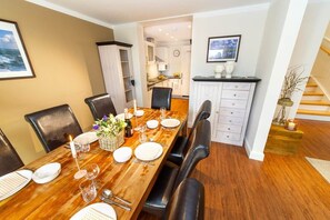 A dining area with a wooden table set for four, a kitchen in the background, and a staircase leading to another level.