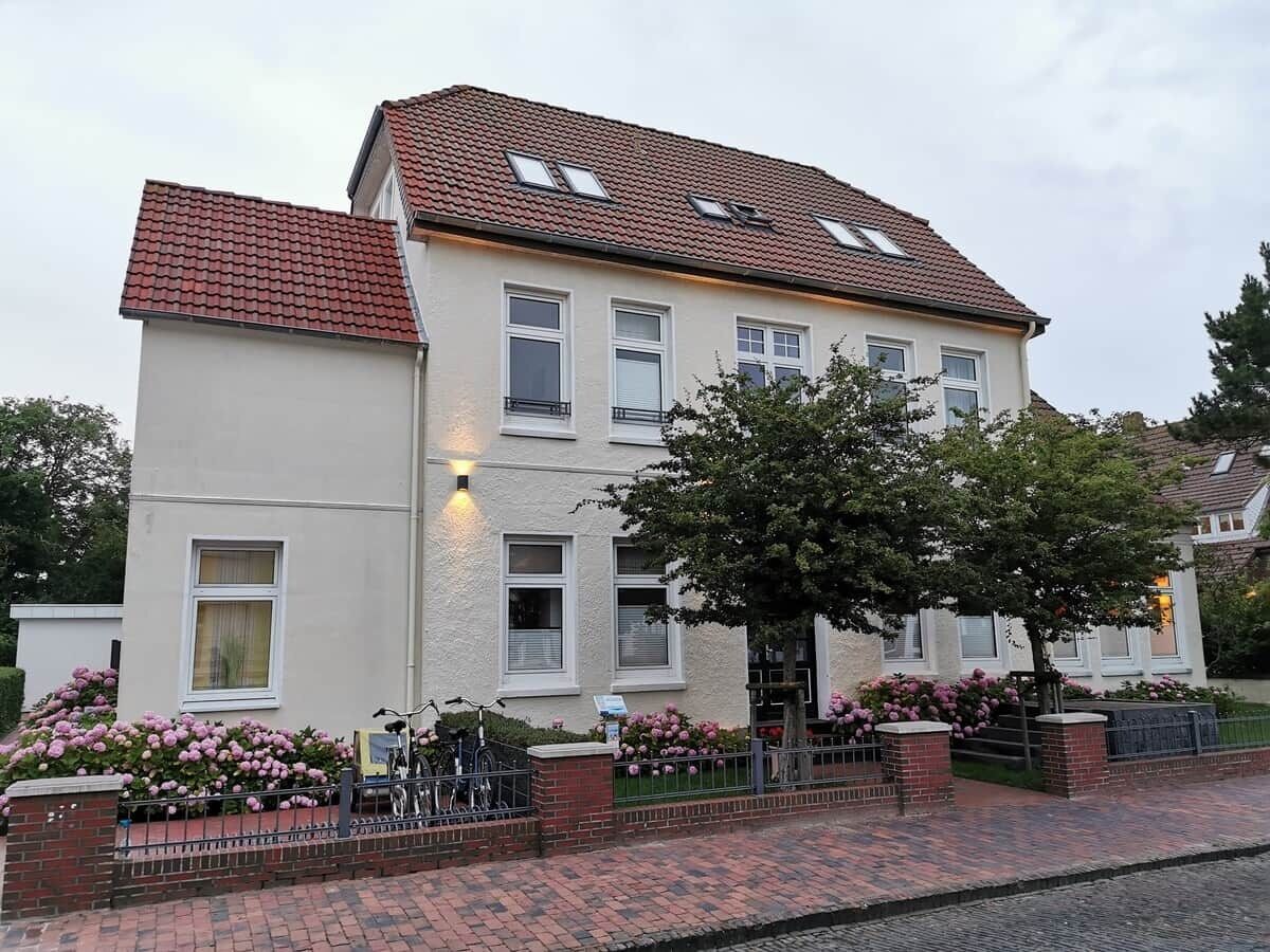 Een woonhuis met twee verdiepingen, een rode dakbedekking van tegels, meerdere ramen en een met baksteen bestraat pad naar de ingang.