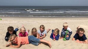 Un groupe d’enfants est allongé sur une plage de sable, avec l’océan en arrière-plan.
