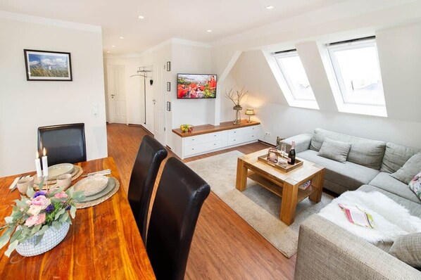 Een moderne woonkamer met een bank, een bijzettafeltje en een eethoek met een tafel gedekt voor twee personen.