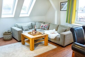 Ein Wohnzimmer mit einer Couch, einem Holztisch, einem Fenster mit Vorhängen und einem gerahmten Bild an der Wand.