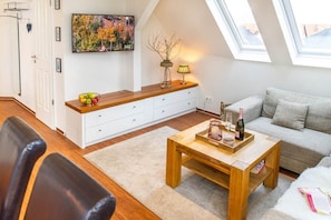 Een moderne woonkamer met een houten salontafel, een bank, een wit kastje en een schilderij aan de muur.