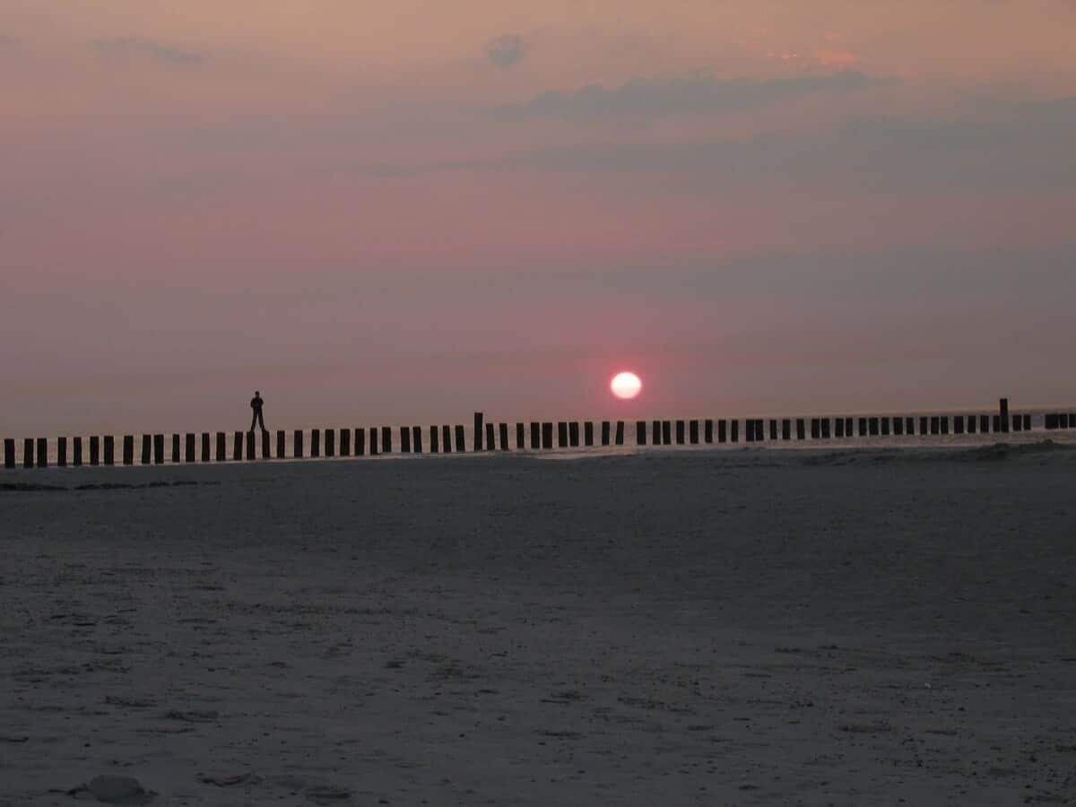 Een strand met iemand die over een houten steiger loopt.