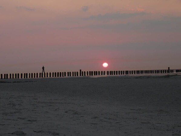 A beach with a person walking along a wooden pier.