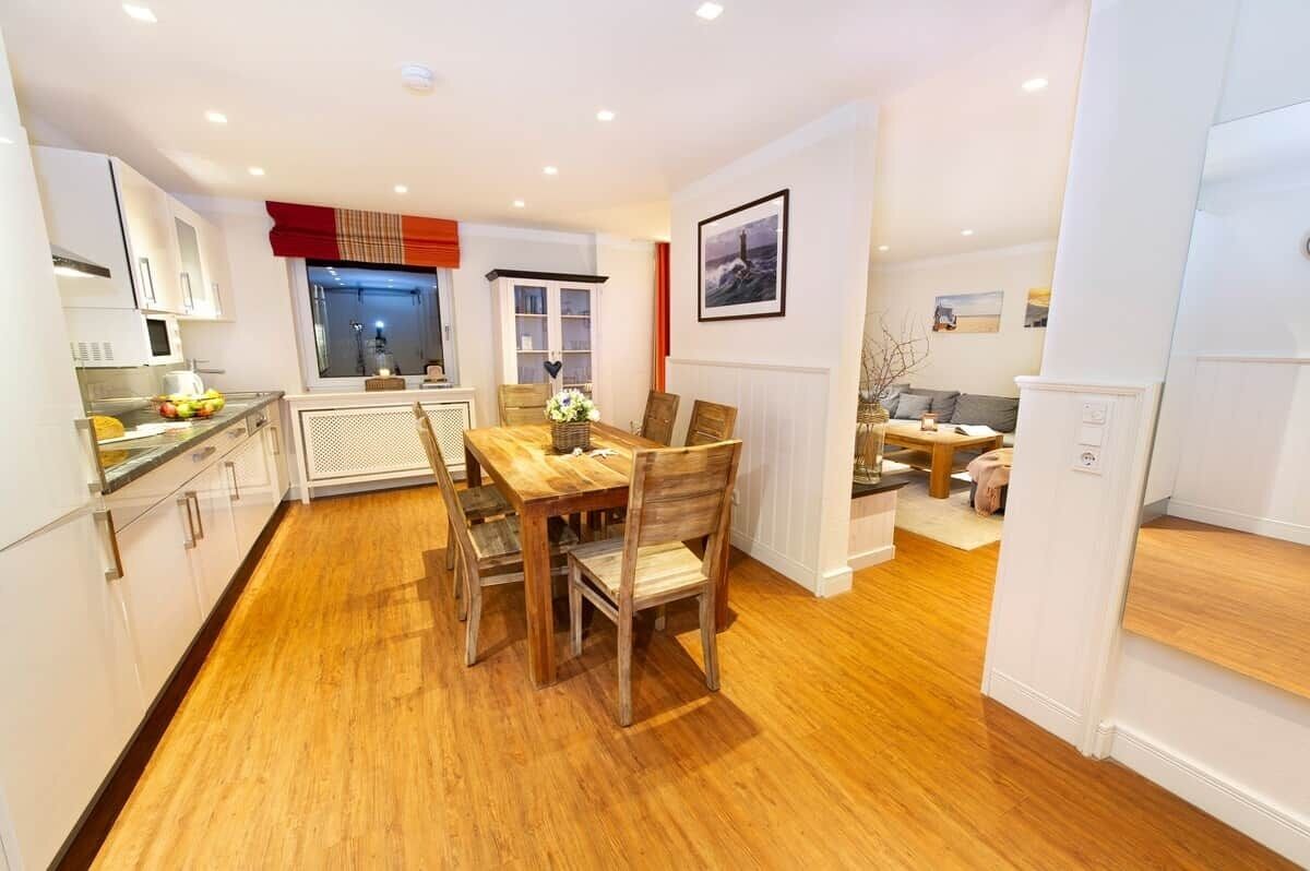 Une cuisine moderne avec un plancher en bois, des meubles blancs et un coin repas comprenant une table et des chaises.