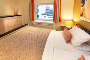 A bedroom with a bed, a dresser, a window with curtains, a lamp, and a wall-mounted picture.