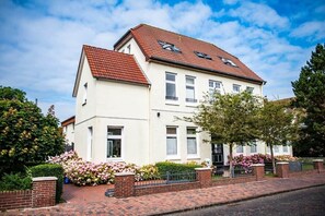 A two-story residential building with a red-tiled roof, white walls, and a brick pathway leading to the entrance.