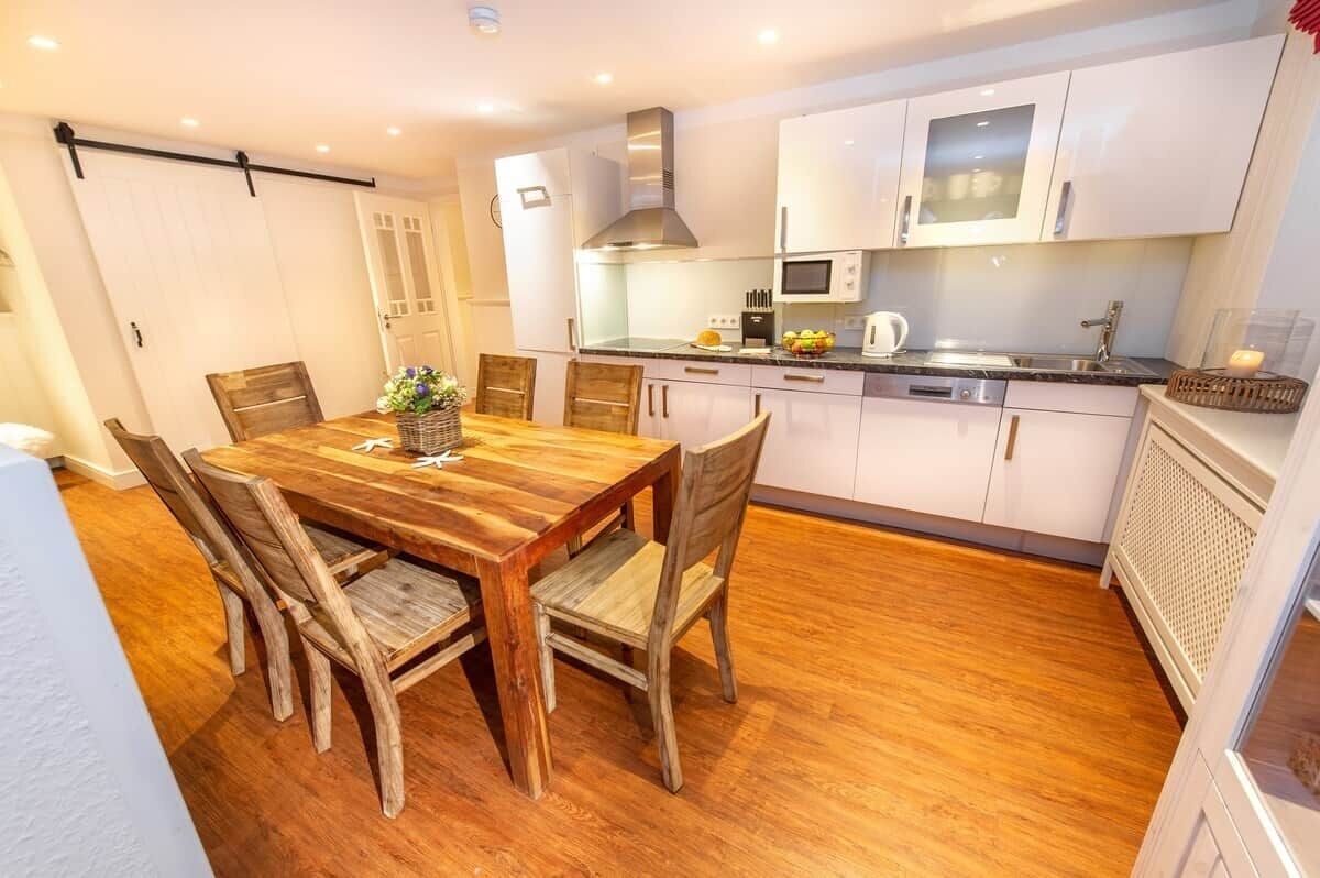 Una cocina moderna con armarios blancos, electrodomésticos de acero inoxidable y una mesa de comedor de madera con sillas.
